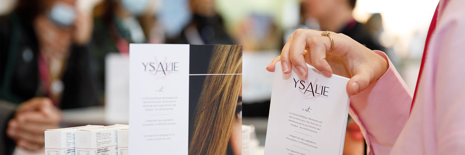 Une main de femme tenant un flyer Ysalie sur lequel est écrit l'histoire d'Ysalie Beauté